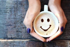 two hands holding a coffee mug with a smile drawn in the foam