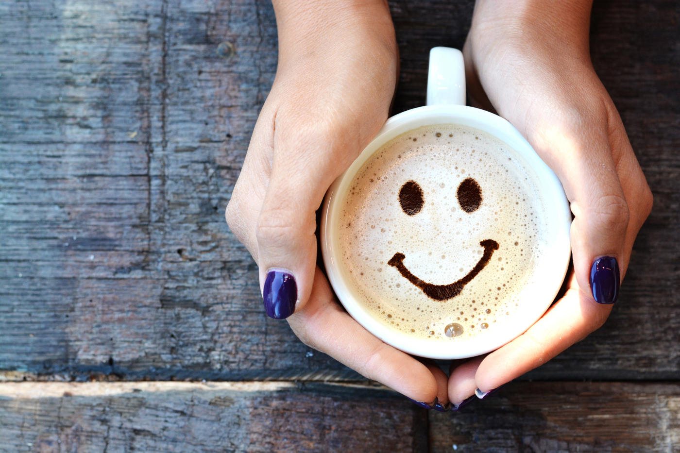 A happy face made from milk foam is seen in a mug of coffee